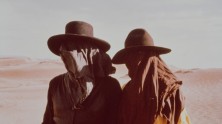 two figures in the desert wearing hats, their faces covered by cloths